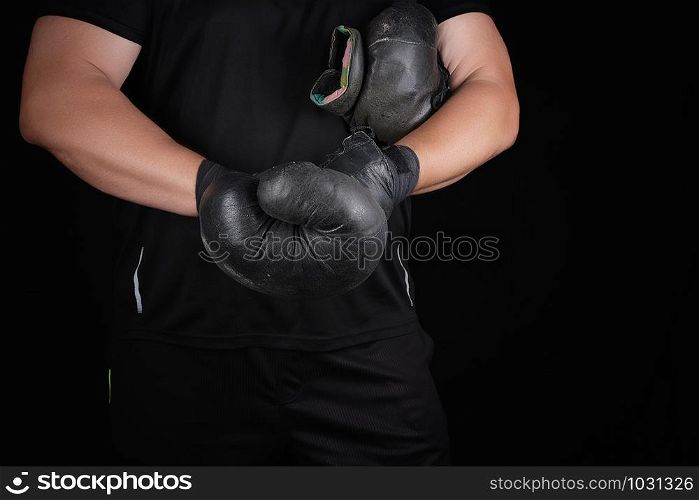 adult muscular man in black clothes puts on leather black boxing gloves on his hands before a competition, his hands are wrapped in a black sports bandage