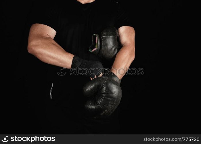 adult muscular man in black clothes puts on leather black boxing gloves on his hands before a competition, his hands are wrapped in a black sports bandage.