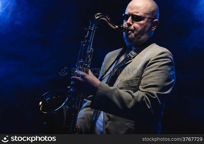 Adult musician playing tenor saxophone, blue smoky background