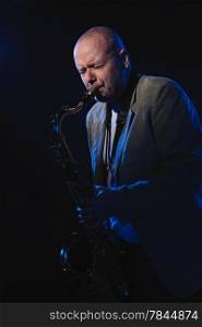 Adult musician playing tenor saxophone, blue smoky background