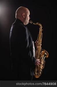 Adult musician playing tenor saxophone, dark background