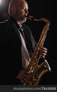 Adult musician playing tenor saxophone eyes closed, dark background