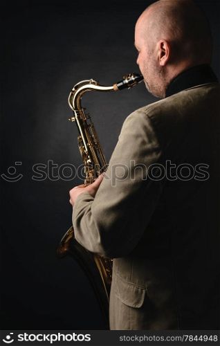 Adult musician playing tenor saxophone, over the shoulder view, dark background