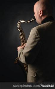 Adult musician playing tenor saxophone, over the shoulder view, dark background