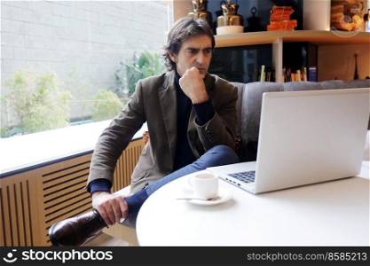 Adult pensive man using laptop in a cafe bar