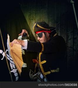 Adult pirate captain in a traditional costume and with arms looks at a treasure map against the backdrop of a jolly roger. Mature Pirate Capitan