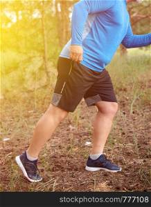 adult plump athlete in blue uniform, sneakers and black shorts runs through the middle of the woods on a summer evening, concept of outdoor sports and a healthy lifestyle