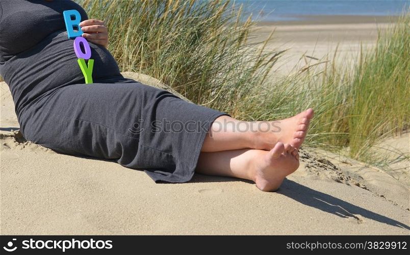 adult pregnant woman holding her hands on her belly on the beach with sand and sea