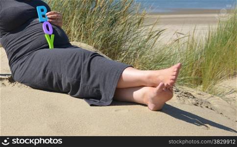 adult pregnant woman holding her hands on her belly on the beach with sand and sea