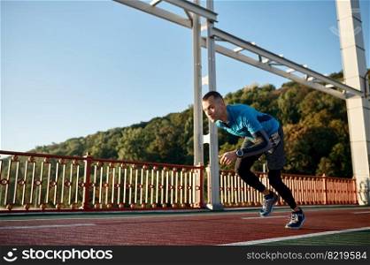 Adult speed runner starting to run on outdoor treadmill racetrack. Training workout, sprinting exercise concept. Adult speed runner running on racetrack
