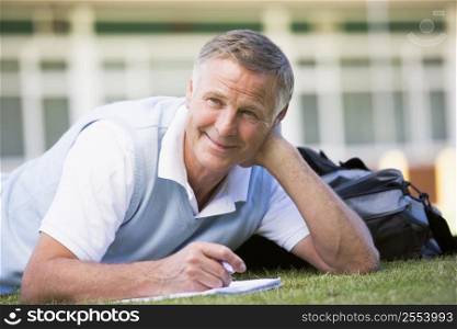 Adult student lying on lawn of school with notebook
