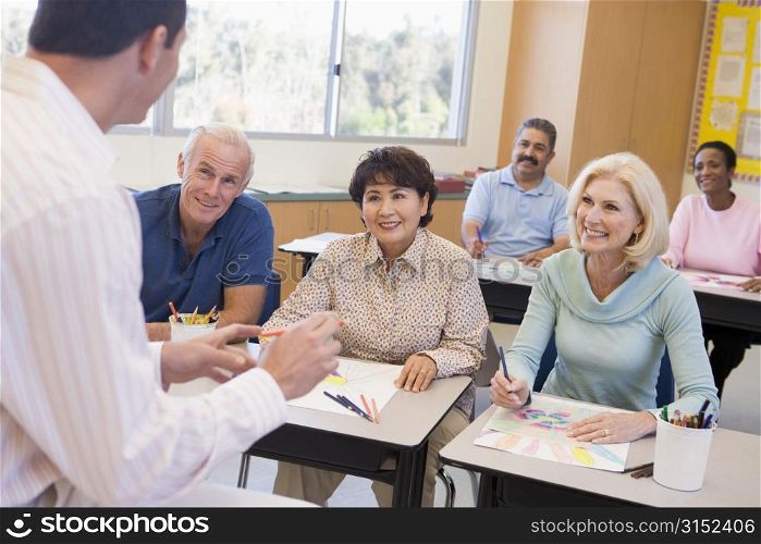 Adult students in class drawing pictures with teacher in foreground (selective focus)