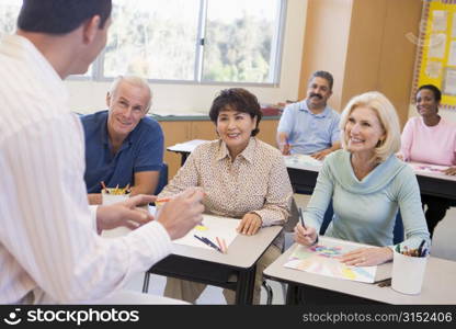 Adult students in class drawing pictures with teacher in foreground (selective focus)