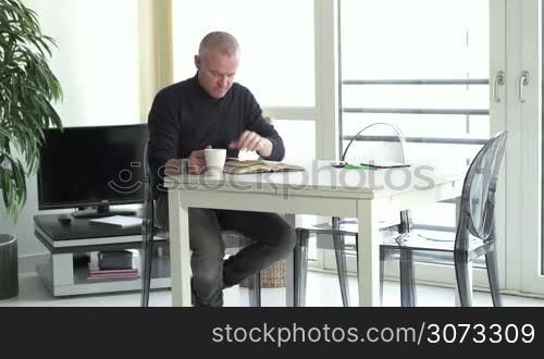 Adult white man relaxing at home reading book for fun and pleasure, sitting and studying in living room in modern apartment. Happy caucasian people leisure, lifestyle, free time, relax