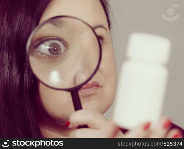 Adult woman investigating ingredients of medicines, chemicals used in pills capsules inside white box. Female using magnifying glass. Woman investigating ingredients of medicines