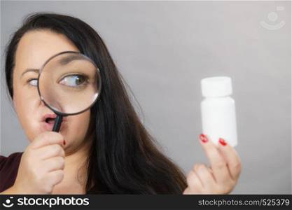 Adult woman investigating ingredients of medicines, chemicals used in pills capsules inside white box. Female using magnifying glass. Woman investigating ingredients of medicines