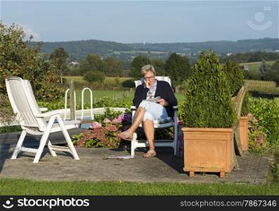 adult woman reading a book near the swimming pool and the belgium hills as background