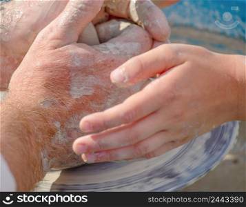 Adults and children&rsquo;s hands over the potter&rsquo;s wheel. The child learns to make a product from clay. Adults and children&rsquo;s hands over the potter&rsquo;s wheel