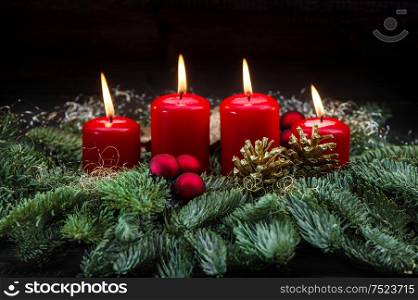 Advent decoration four red burning candles, baubles and christmas tree branches