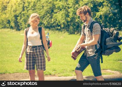 Adventure, tourism, enjoying summer time together - Hiking young couple with guitar backpack tramping on forest road sunny countryside