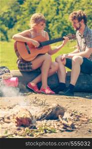 Adventure, tourism, enjoying summer time together - young couple tourists having fun playing guitar in camping outdoor