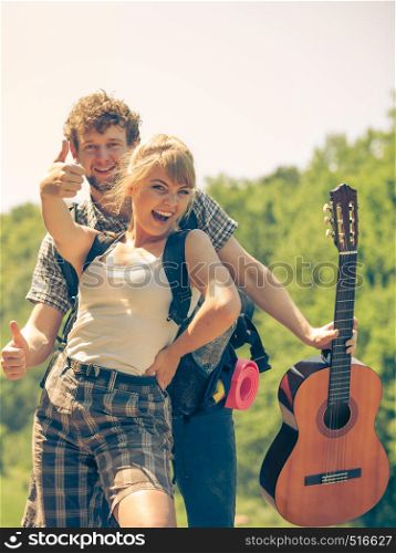 Adventure, tourism, enjoying summer time together - young couple tourists hikers with guitar having fun showing thumb up sign outdoor