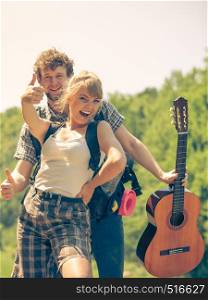 Adventure, tourism, enjoying summer time together - young couple tourists hikers with guitar having fun showing thumb up sign outdoor