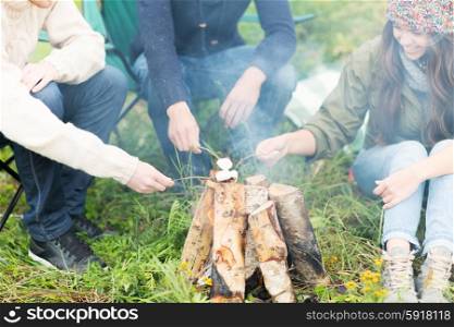 adventure, travel, tourism and people concept - close up of happy friends hikers roasting marshmallow on fire