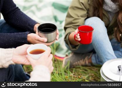 adventure, travel, tourism and people concept - close up of hikers drinking tea from cups at camp