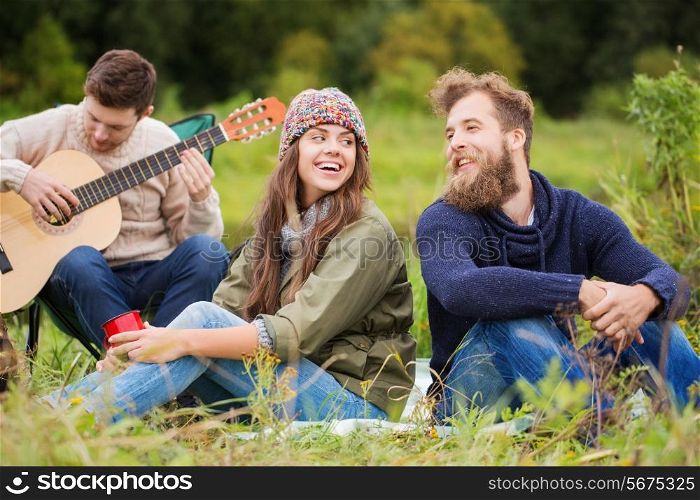 adventure, travel, tourism and people concept - group of smiling friends with guitar in camping