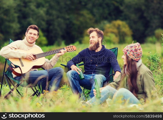 adventure, travel, tourism and people concept - group of smiling tourists playing guitar and drinking beer in camping