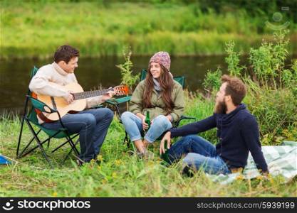 adventure, travel, tourism and people concept - group of smiling tourists playing guitar and drinking beer in camping