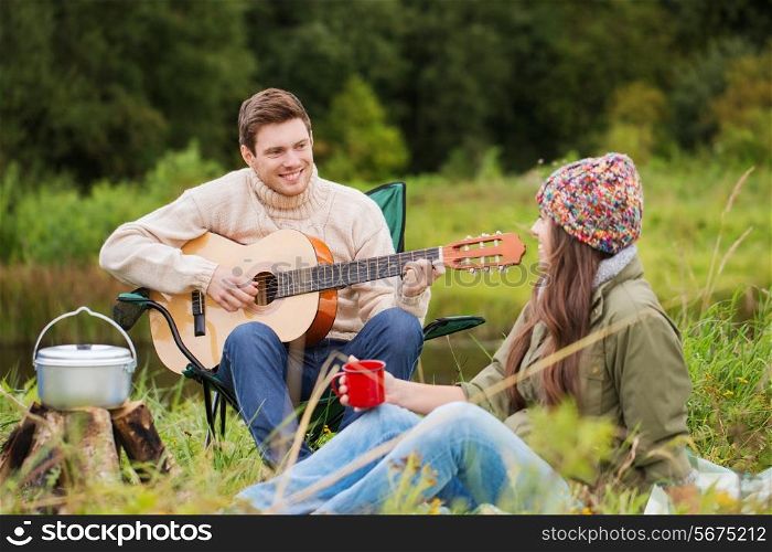 adventure, travel, tourism and people concept - smiling couple with guitar cooking food and drinking in camping