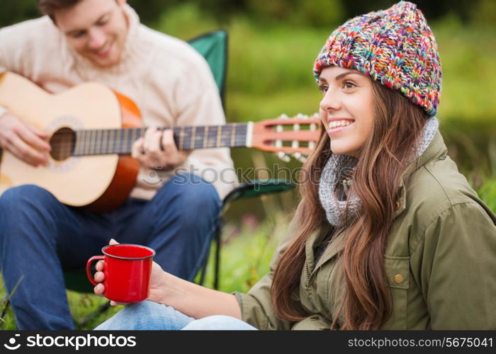 adventure, travel, tourism and people concept - smiling couple with guitar in camping