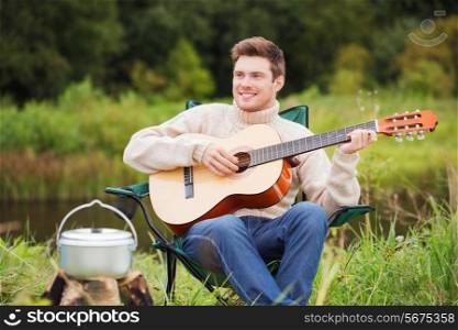 adventure, travel, tourism and people concept - smiling man with guitar and cooking food on bonfire in camping