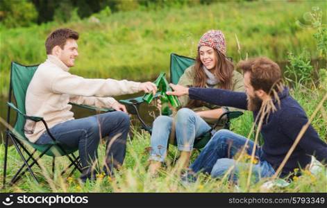 adventure, travel, tourism, friendship and people concept - group of smiling tourists clinking beer bottles in camping