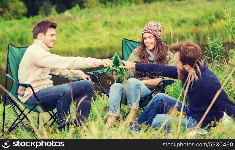 adventure, travel, tourism, friendship and people concept - group of smiling tourists clinking beer bottles in camping