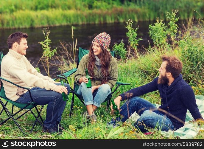 adventure, travel, tourism, friendship and people concept - group of smiling tourists drinking beer in camping