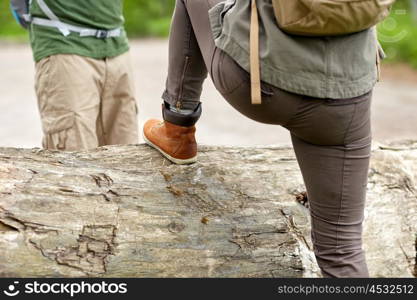 adventure, travel, tourism, hike and people concept - close up of couple with backpacks walking and climbing over fallen tree trunk in woods. close up of couple with backpacks hiking