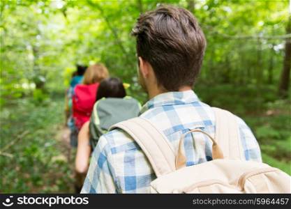adventure, travel, tourism, hike and people concept - close up of friends walking with backpacks in woods from back
