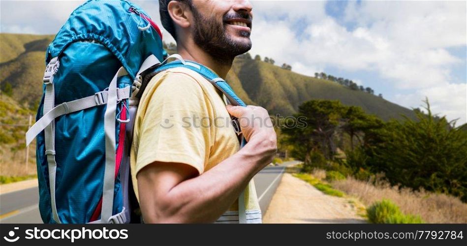 adventure, travel, tourism, hike and people concept - close up of smiling young man with backpack over big sur hills and road of california background. close up of man with backpack over big sur hills