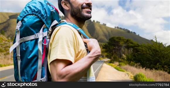 adventure, travel, tourism, hike and people concept - close up of smiling young man with backpack over big sur hills and road of california background. close up of man with backpack over big sur hills