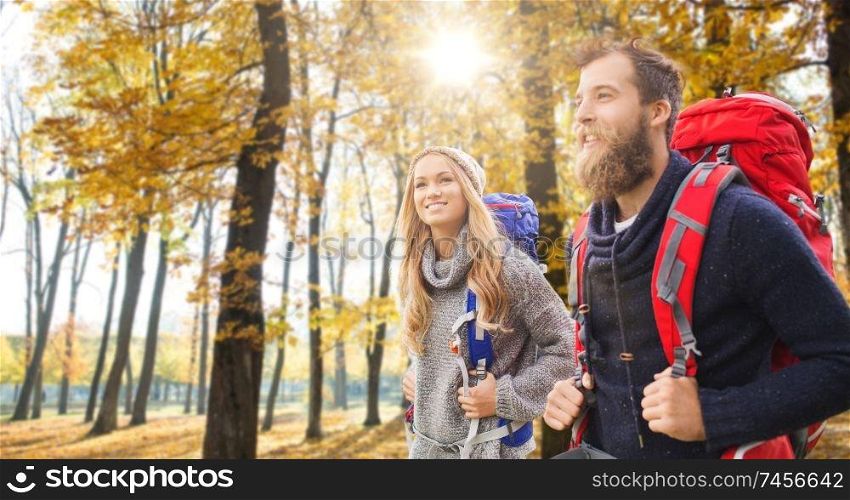 adventure, travel, tourism, hike and people concept - couple of travelers with backpacks over autumn park background. smiling couple with backpacks hiking in autumn