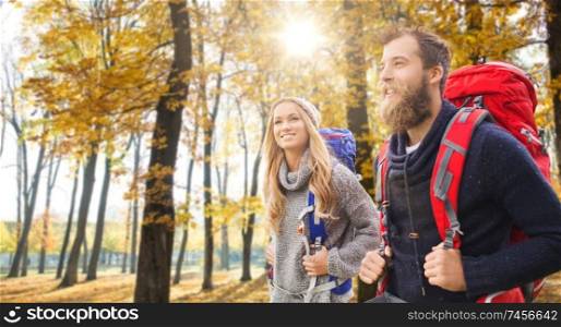 adventure, travel, tourism, hike and people concept - couple of travelers with backpacks over autumn park background. smiling couple with backpacks hiking in autumn