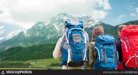 adventure, travel, tourism, hike and people concept - group of friends walking with backpacks from back over alps mountains background