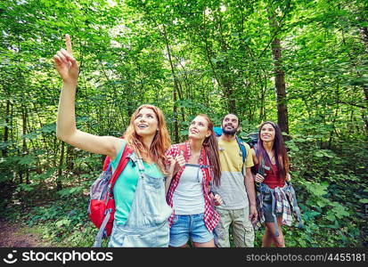 adventure, travel, tourism, hike and people concept - group of smiling friends with backpacks pointing finger up in woods