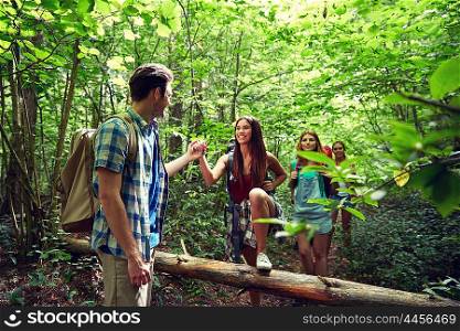 adventure, travel, tourism, hike and people concept - group of smiling friends walking with backpacks and climbing over fallen tree trunk in woods