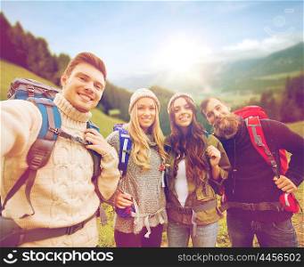 adventure, travel, tourism, hike and people concept - group of smiling friends with backpacks making selfie over alpine mountains and hills background
