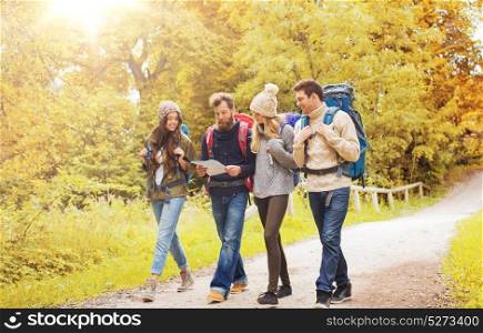 adventure, travel, tourism, hike and people concept - group of smiling friends walking with backpacks and map walking in autumn forest. group of smiling friends with backpacks hiking