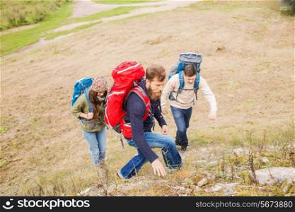 adventure, travel, tourism, hike and people concept - group of smiling friends with backpacks climbing on hill